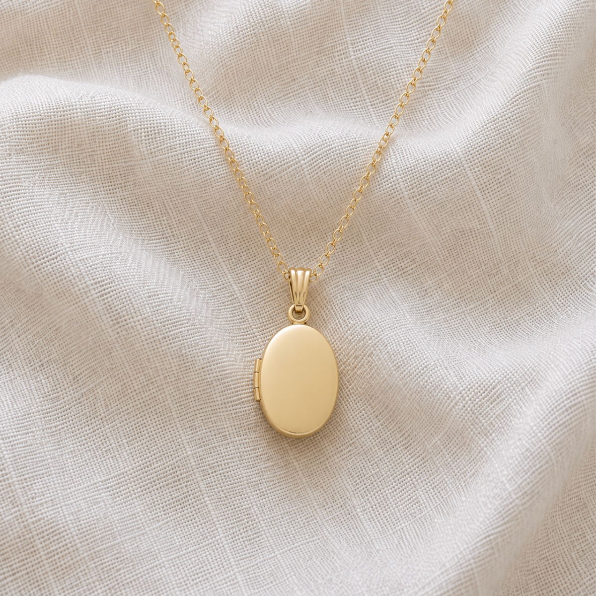 Petite 14K gold-filled oval pet memorial locket on a delicate gold chain, displayed on ivory linen.