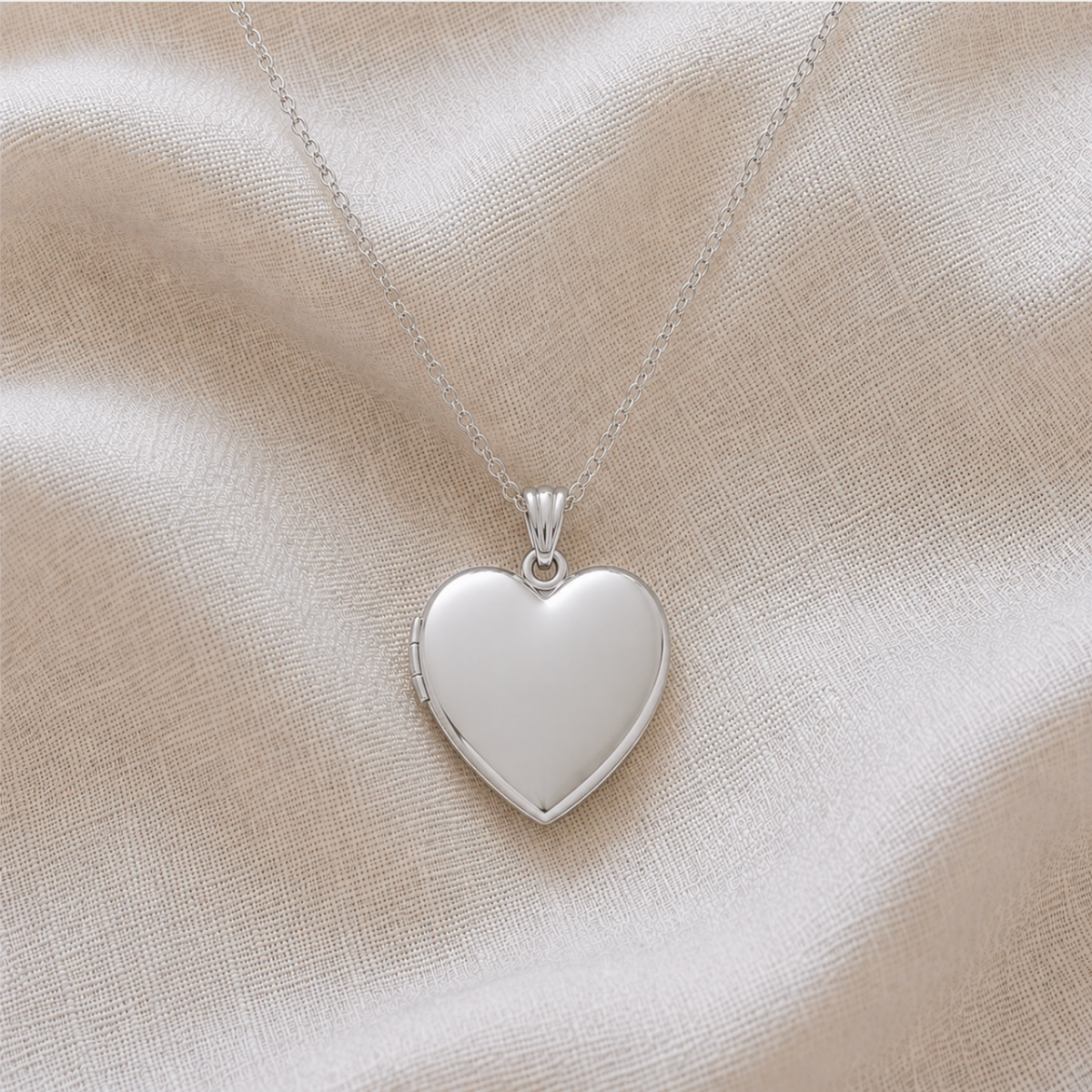 A polished sterling silver heart-shaped locket pet memorial pendant necklace on a delicate silver chain, displayed on a draped linen fabric background.