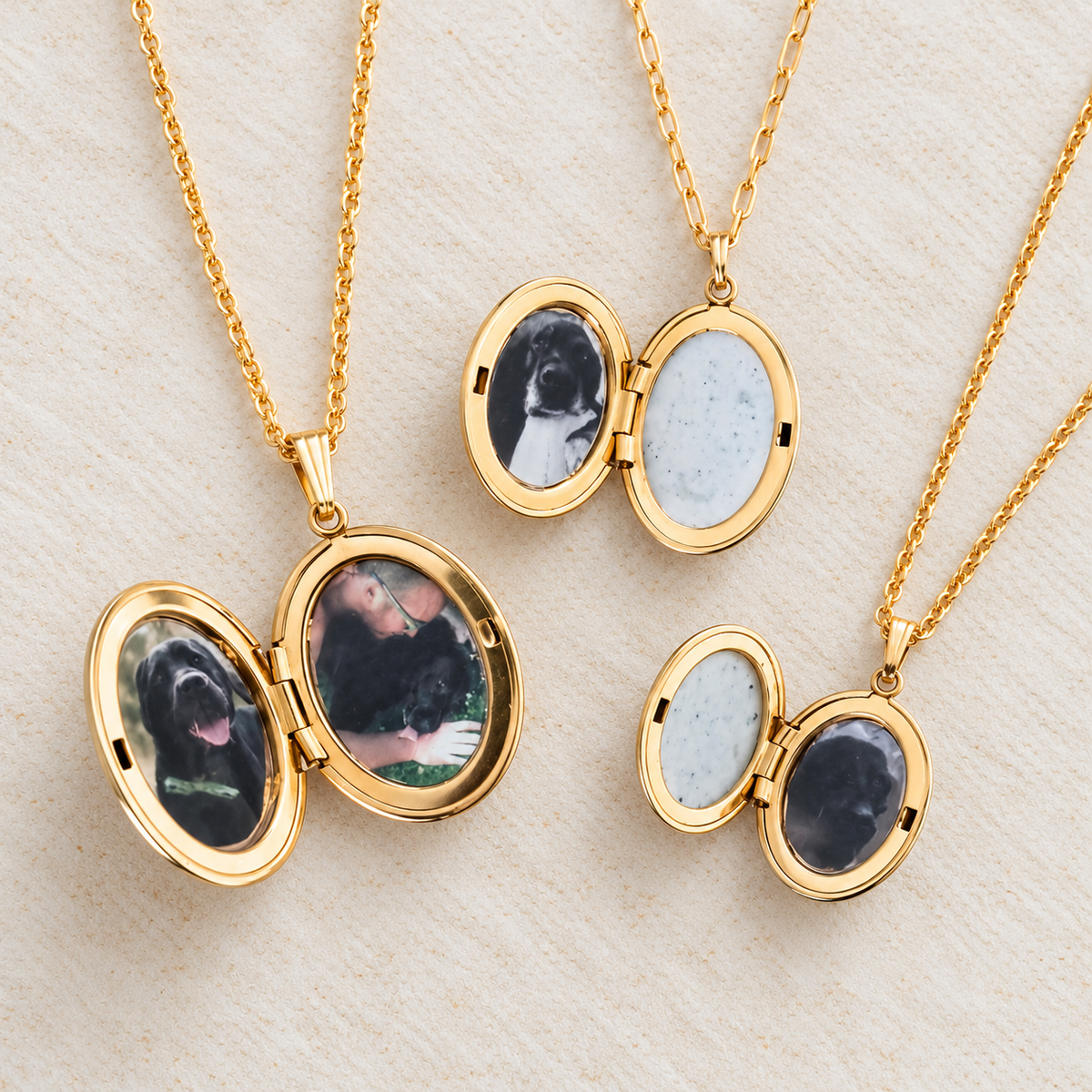 Three gold-tone oval locket necklaces on chains, shown open to reveal custom pet memorial photos and light blue stone inserts, arranged on a light textured background.