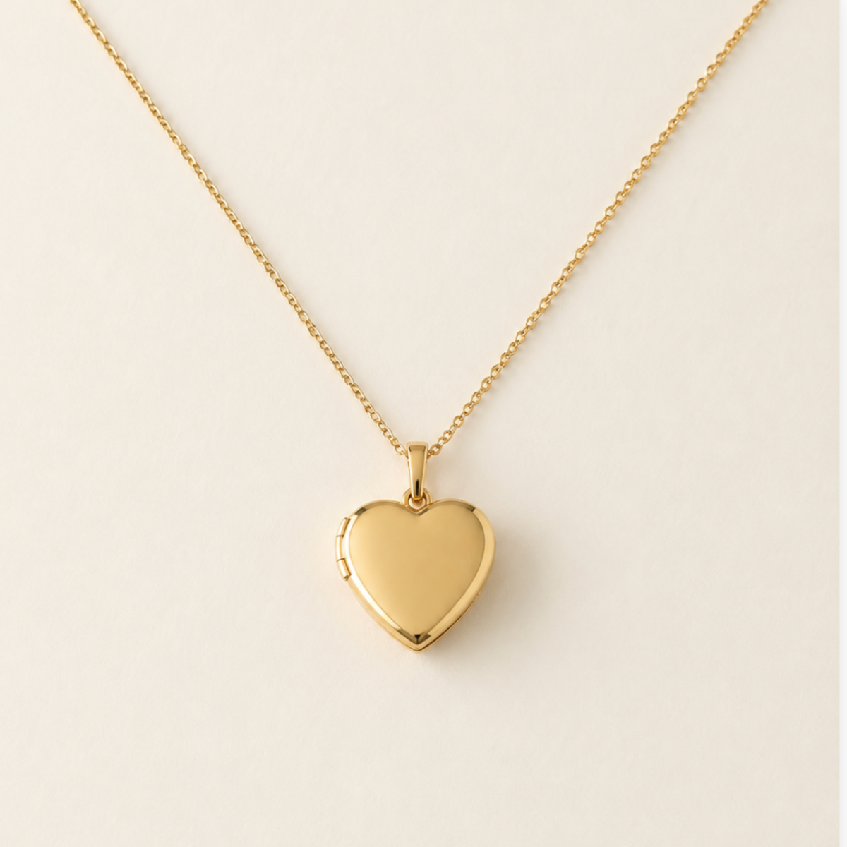 A polished 14k gold filled heart-shaped locket pet memorial  necklace on a delicate gold chain, displayed against a clean, light beige background.