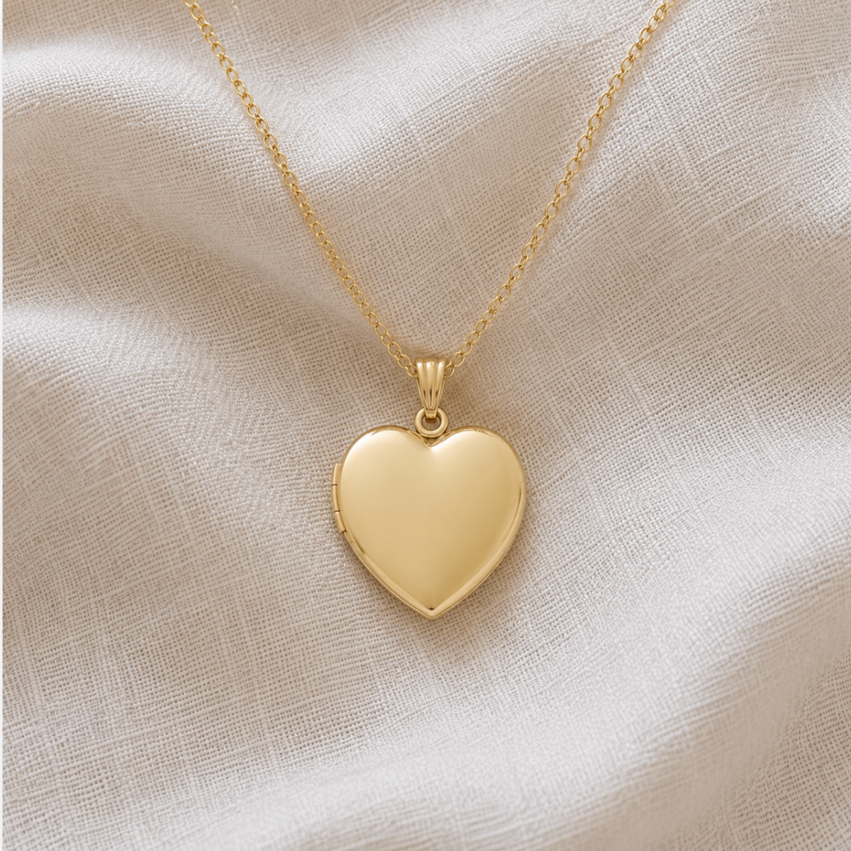 A polished 14k gold filled heart-shaped pet memorial locket necklace on a delicate gold chain, displayed on a textured linen fabric background.